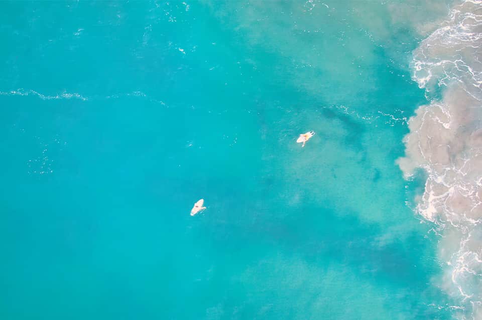Aerial shot of turquoise ocean water with two surfers near shore