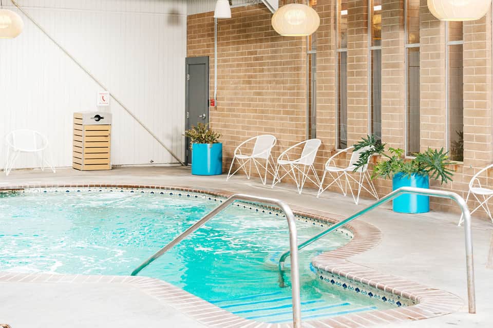 Indoor pool with spa jets, white modern chairs, and brick architecture