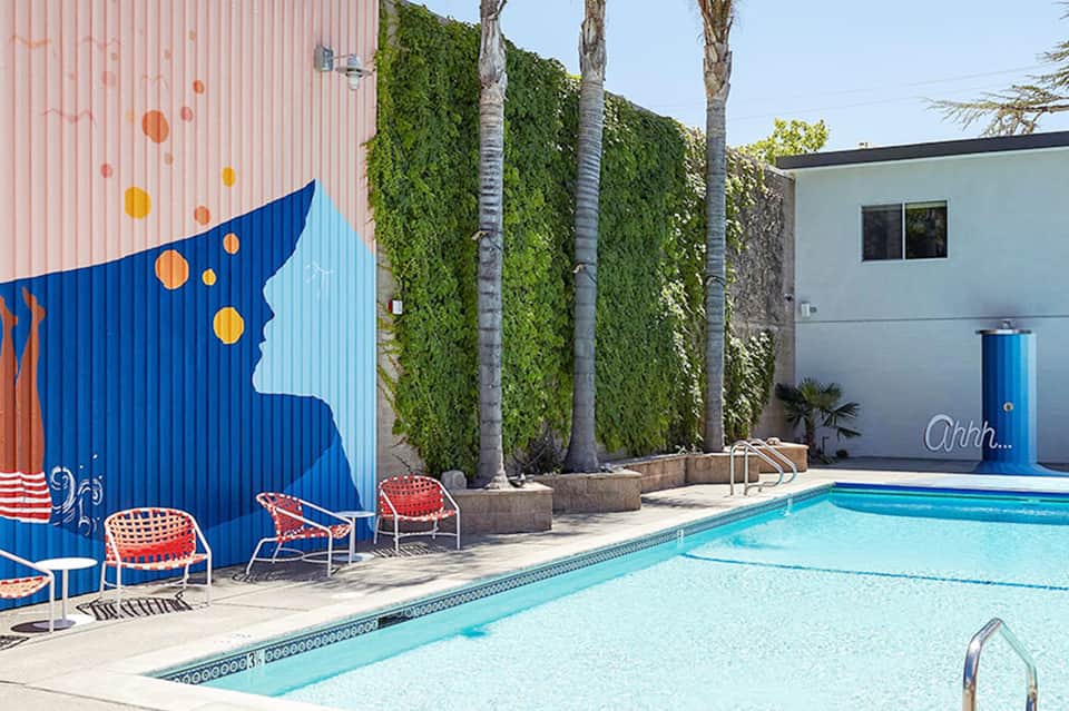 Modern pool area with blue mural art wall, ivy-covered pillars, and colorful lounge chairs