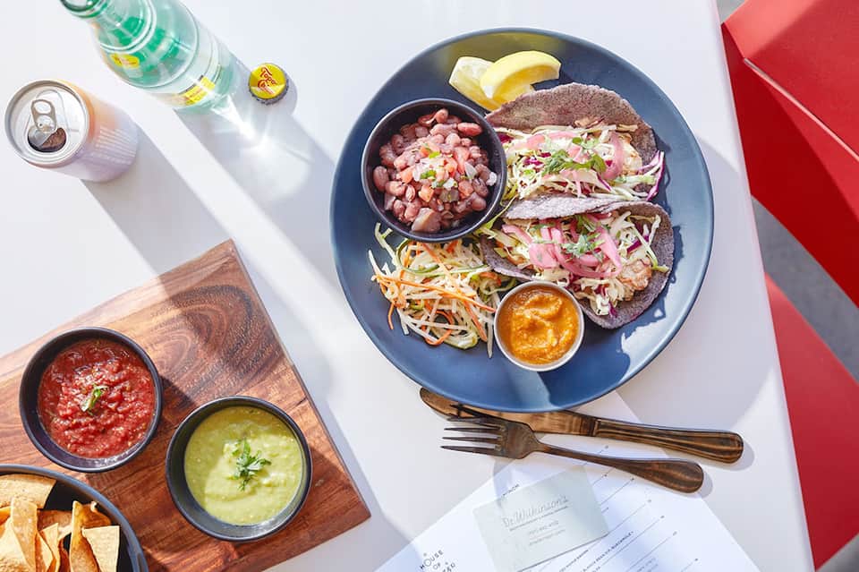 Plate of tacos with ceviche, salsa, and garnishes on blue plate with beverages
