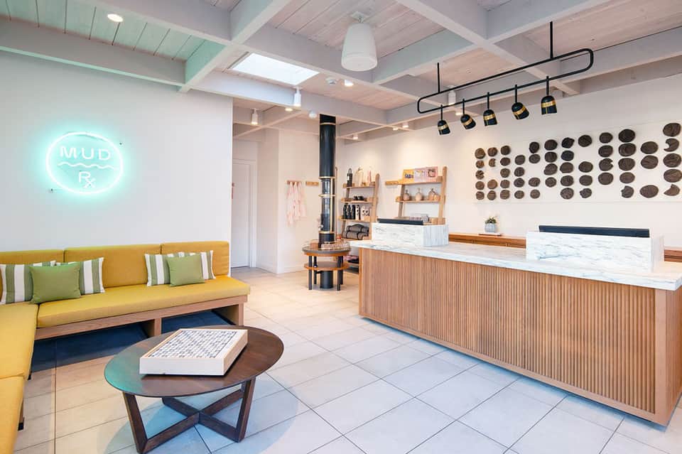 Modern spa reception area with yellow sofa, neon sign, and wooden counter