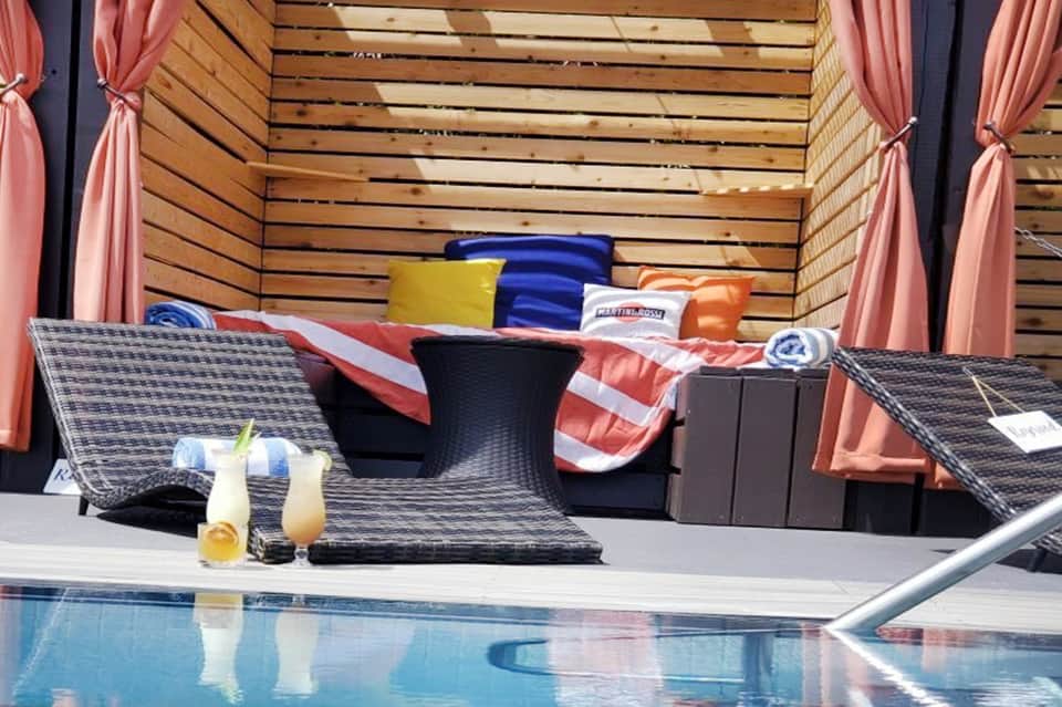 Poolside cabana with pink curtains, colorful pillows, and tropical beverages on table