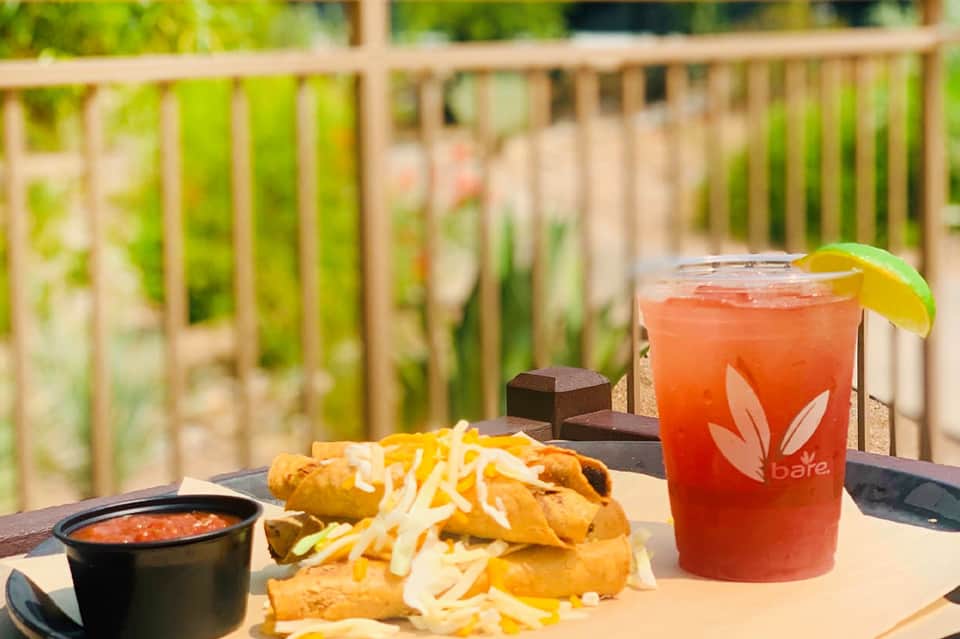 Grilled food and coral-colored drink on table overlooking green landscape