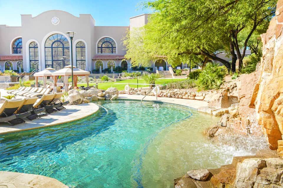 Resort courtyard pool with turquoise water, limestone rocks, and striped lounge chairs under shade pavilion
