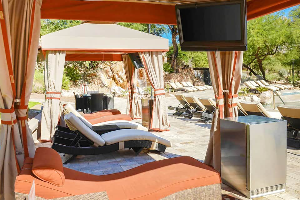 Covered lounge area with orange and white striped fabric cabanas and loungers under pergola