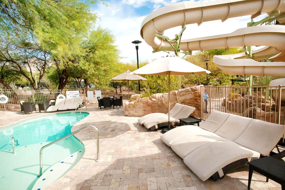 Resort pool area with water slides, loungers, umbrellas, and desert landscaping