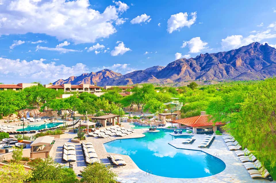 Desert resort pool with loungers, mountains in background, tropical landscaping