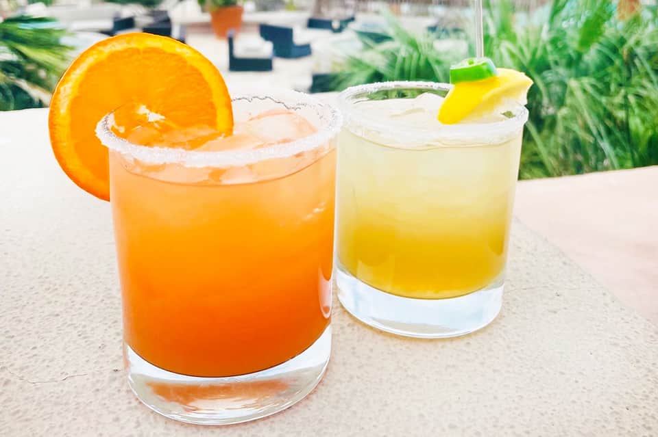 Two colorful cocktails with citrus garnishes served poolside at a resort bar
