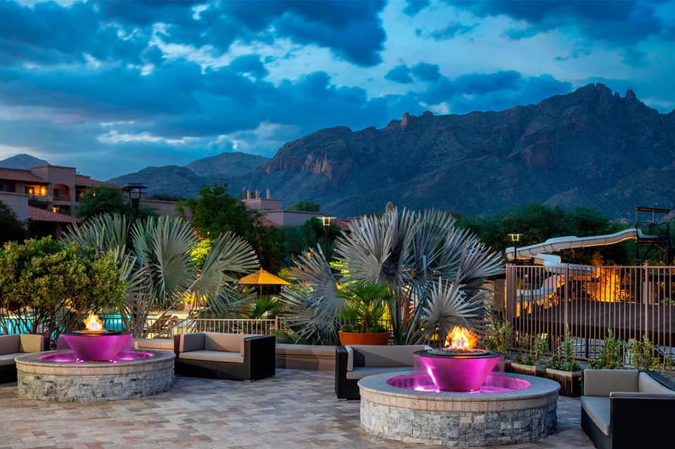 Desert resort courtyard at dusk with fire pits, lounge seating, and mountain backdrop