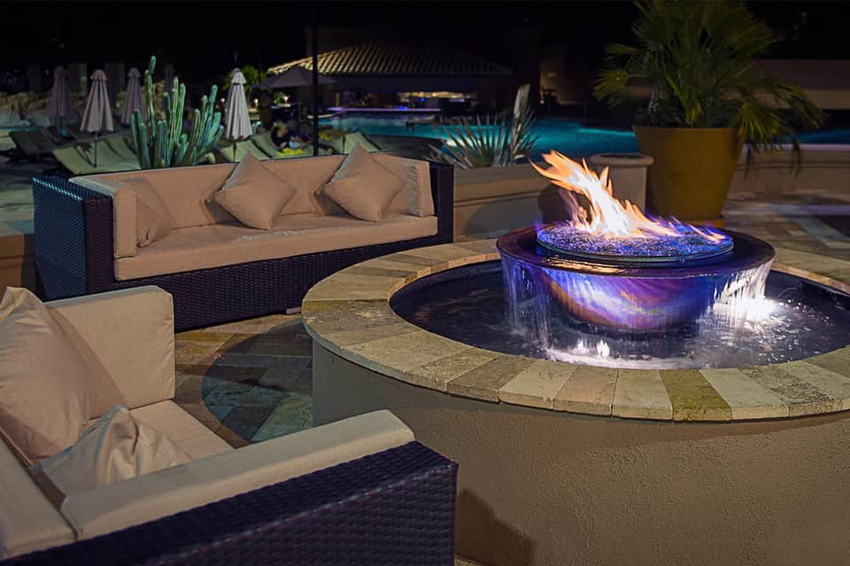 Nighttime resort patio with fire pit, lounge seating, and illuminated pool in background