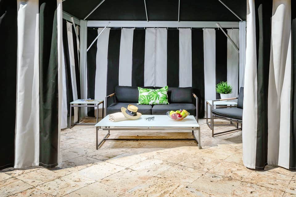 Private cabana on beach with black and white striped curtains, sofa, and white pillows