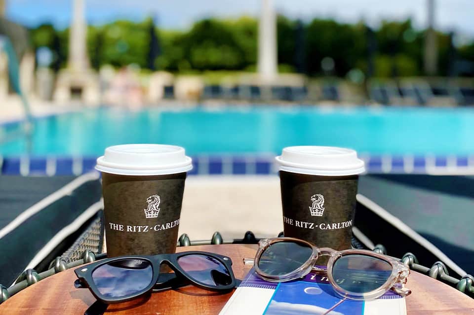 Two Ritz-Carlton coffee cups beside sunglasses overlooking a swimming pool