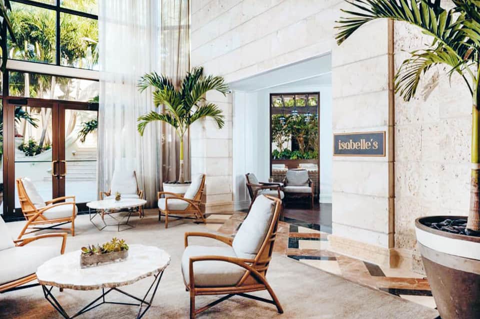 Modern spa lounge with wooden chairs, marble floors, potted palms, and Isabelle's signage