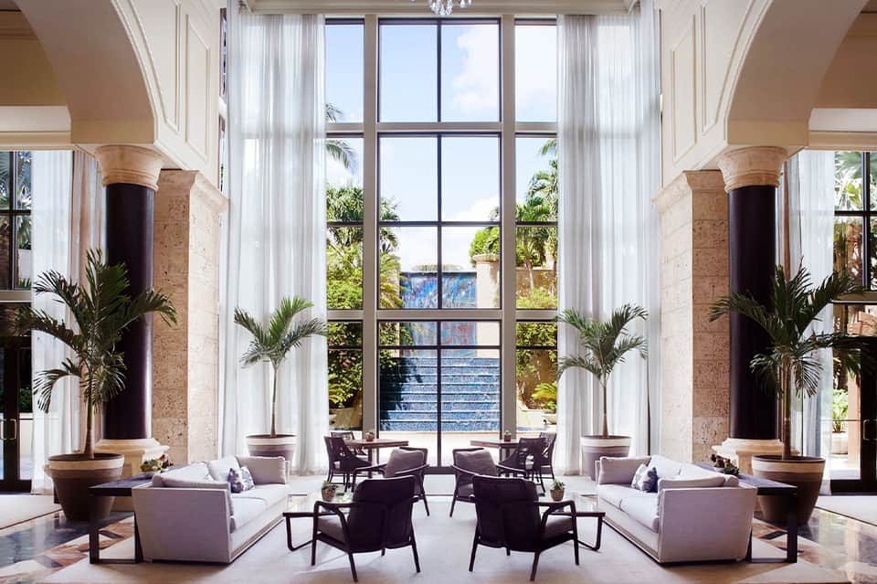 Luxurious resort lobby with towering columns, potted palms, sheer white curtains, and elegant seating areas