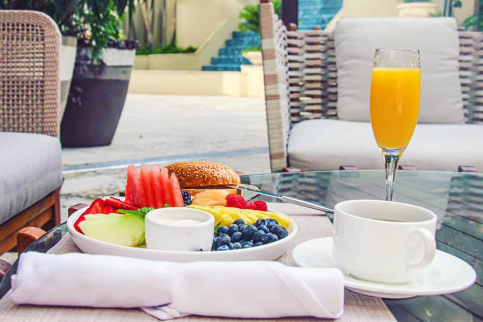 Outdoor dining table with fresh breakfast, fruit plate, sandwich, juice, and resort patio setting