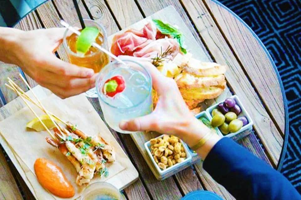 Overhead view of poolside appetizers, drinks with fruit garnish, prosciutto, and snacks