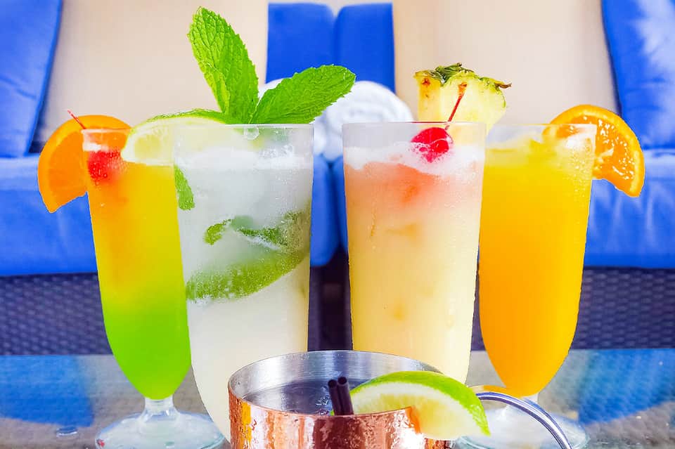 Colorful tropical cocktails with fresh fruit garnishes on blue lounge chairs by pool