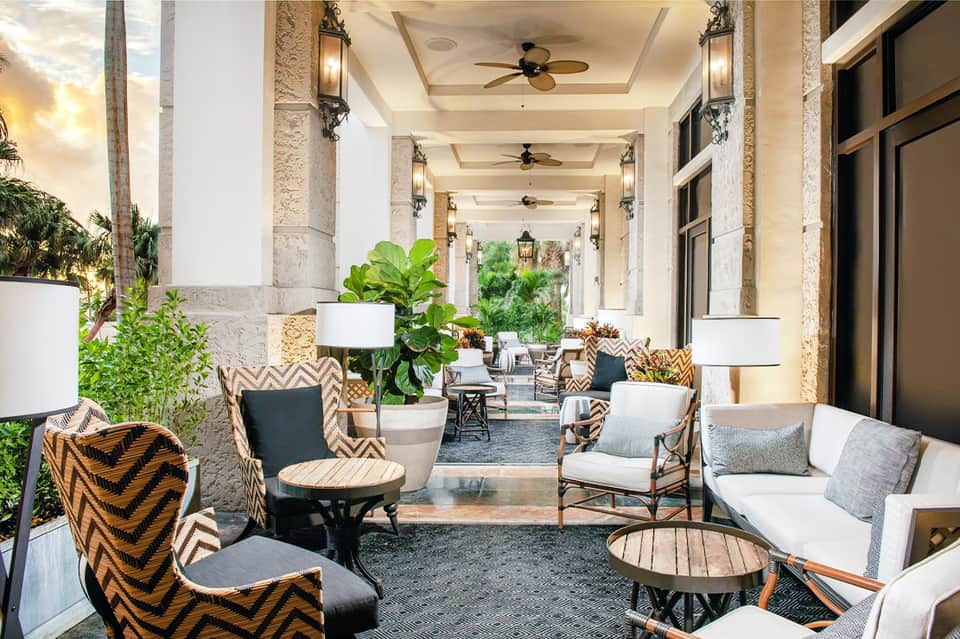 Covered outdoor patio with columns, patterned chairs, potted plants, and lounge seating