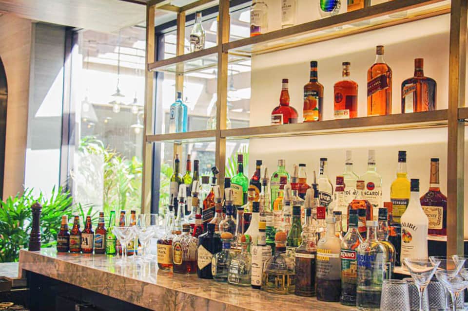 Modern bar with extensive liquor collection on glass shelves and wooden display cabinet