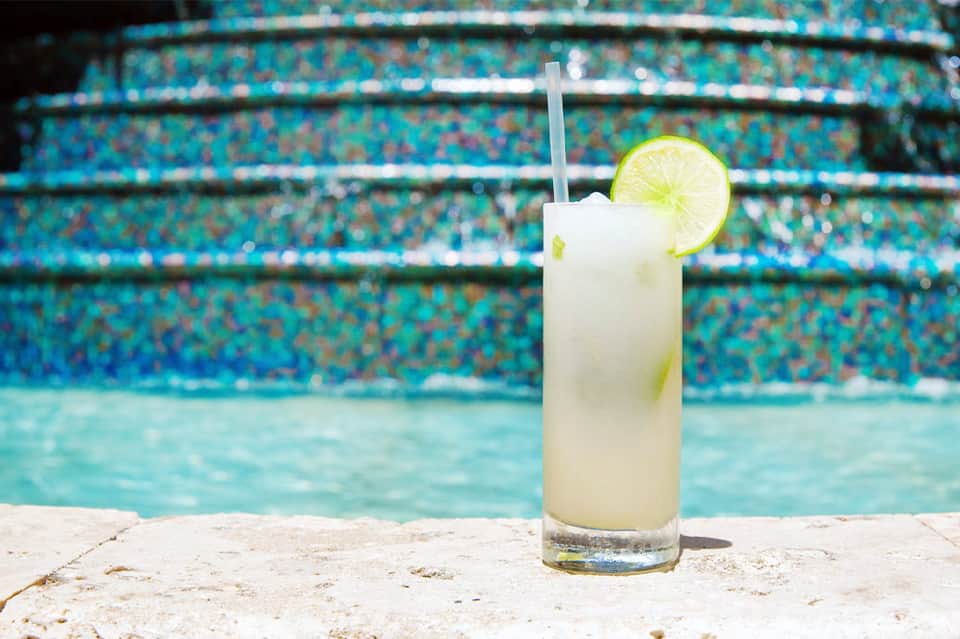 Refreshing cocktail with lime slice at pool edge, clear water and tiled pool deck visible in background