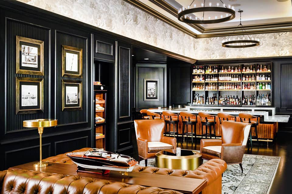 Luxury lounge with cognac leather chairs, black walls, gold accents, and full bar