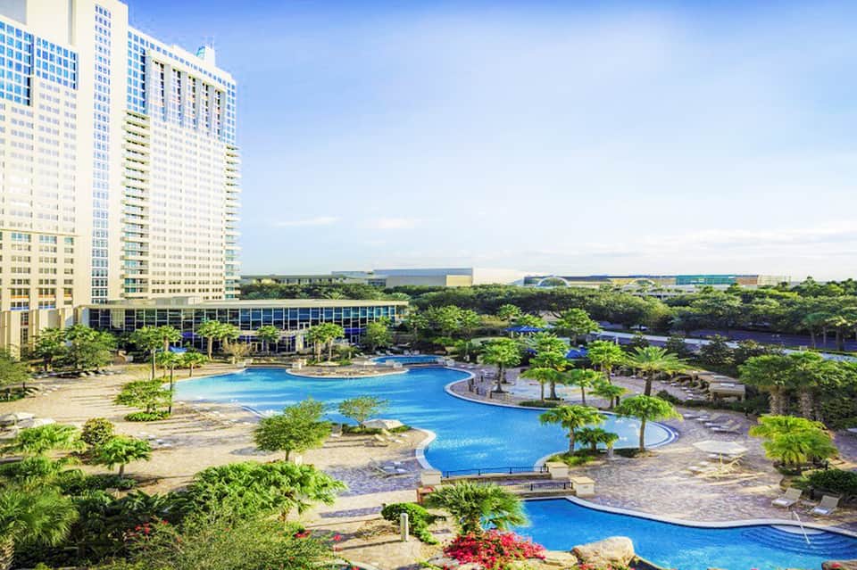 Aerial view of large resort complex with curved blue pools and high-rise building