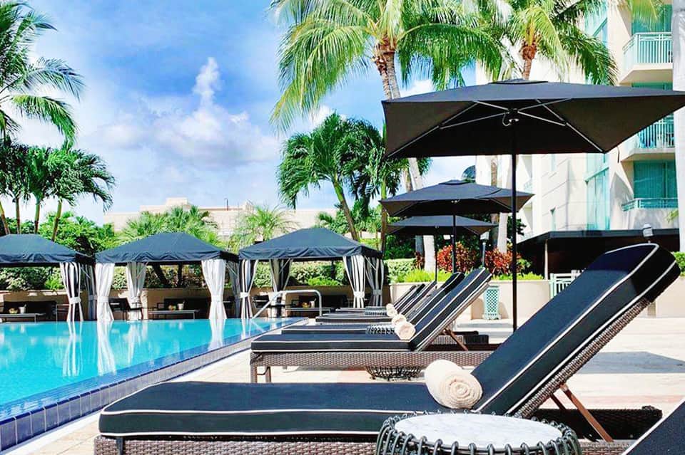 Luxury pool area with black loungers, umbrellas, cabanas, palm trees, and modern hotel building