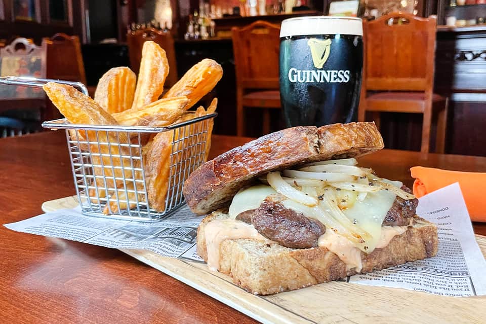 Gourmet sandwich with melted cheese and crispy fries in basket beside Guinness beer in pub setting