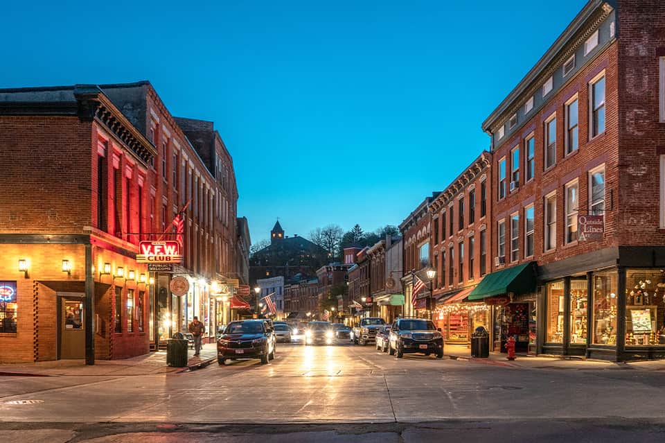 Historic downtown street at dusk with brick buildings, shops, and neon signs