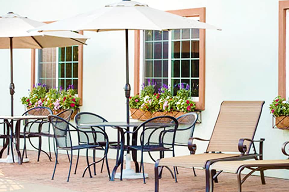 Beachfront patio with white umbrellas, lounge chairs, flowering planters, and ocean view
