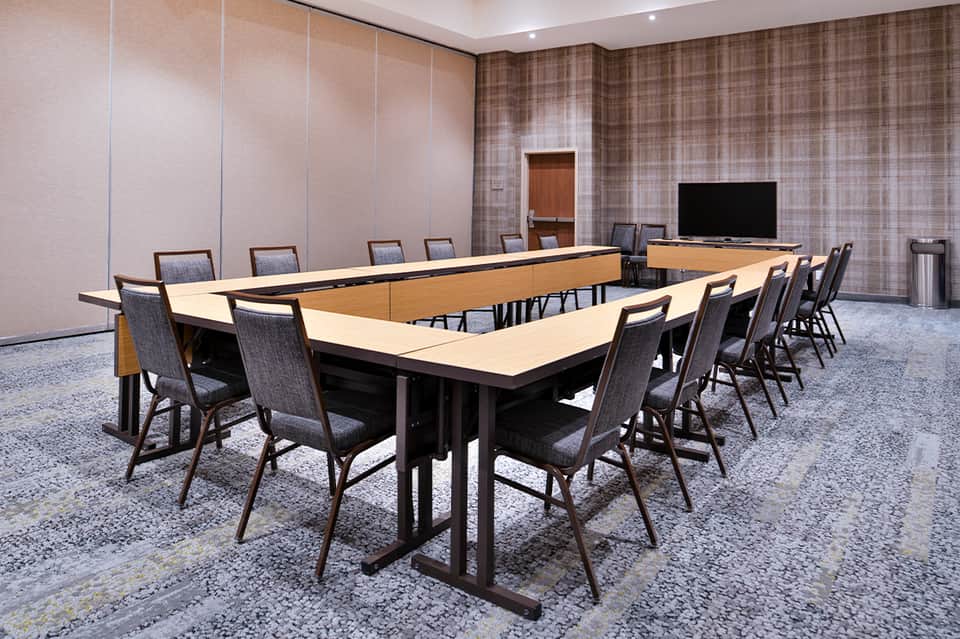 U-shaped conference table with chairs in meeting room with patterned walls and wall-mounted TV