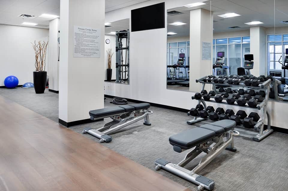 Modern fitness center with dumbbells, weight benches, exercise equipment, and mirrors