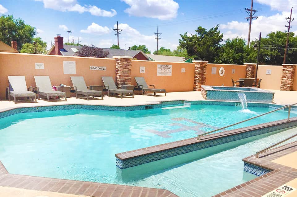Bright turquoise swimming pool with spa jets and lounge chairs against tan accent wall