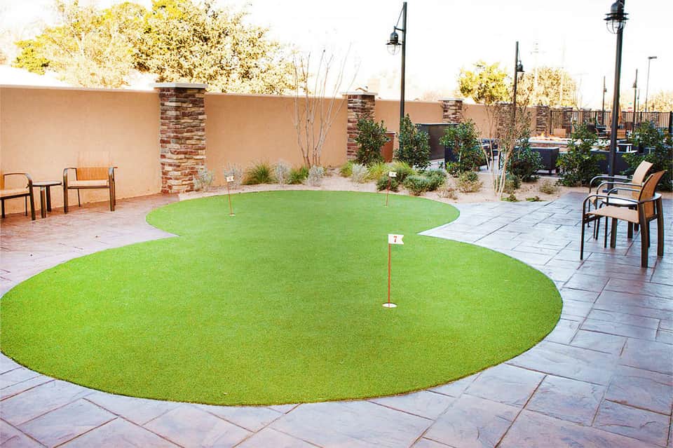 Mini golf course with two green circular putting areas on resort patio with seating