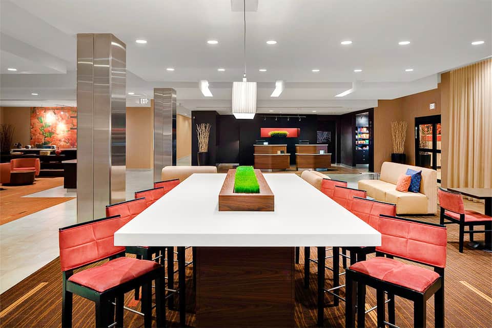 Contemporary event space with long white table, red accent chairs, black and wood elements, and warm lighting