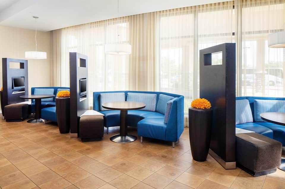 Modern hotel lounge with blue curved seating, dark accent pillars, and floor-to-ceiling windows