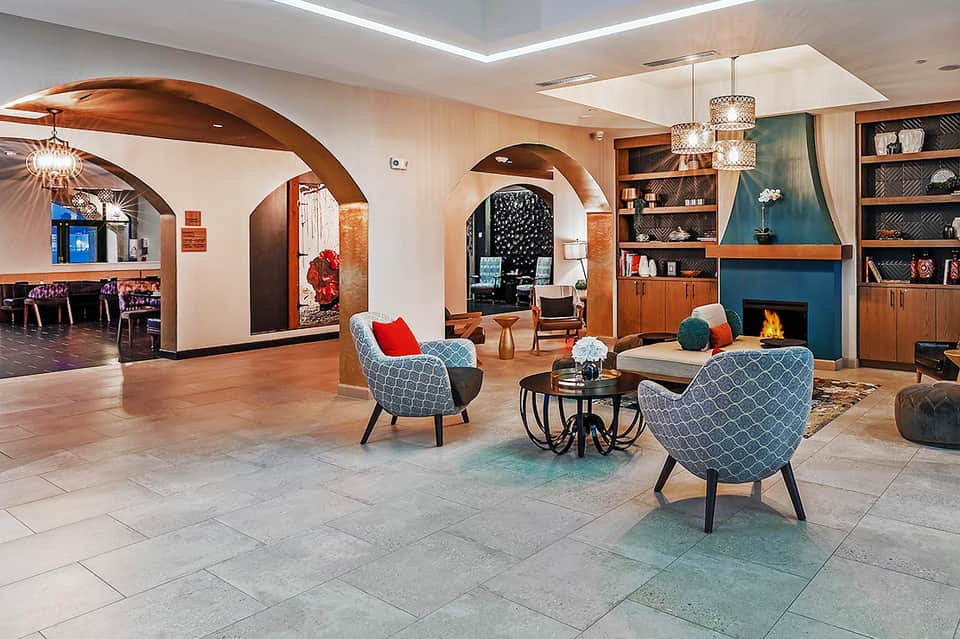 Modern resort lobby with arched wooden ceilings, fireplace, geometric armchairs, and built-in shelving.