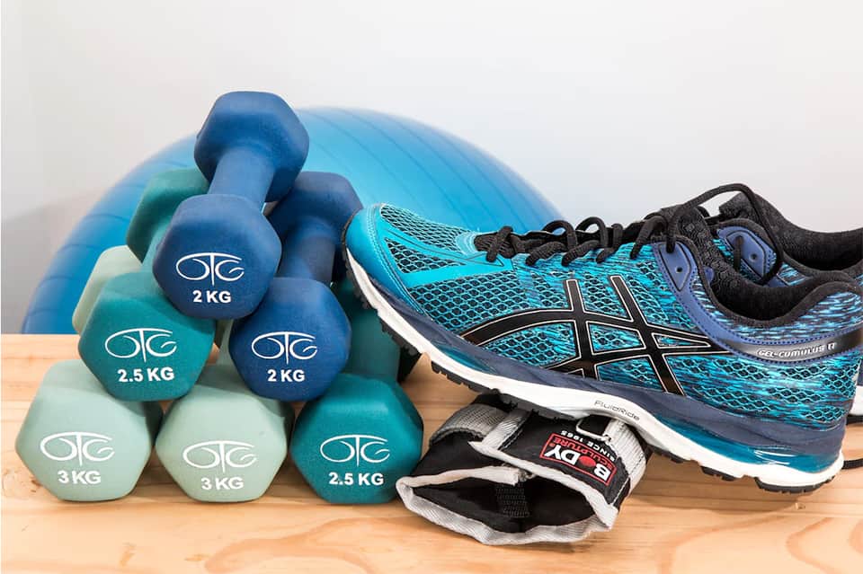 Fitness equipment including blue dumbbells, running shoes, and exercise ball on wooden floor