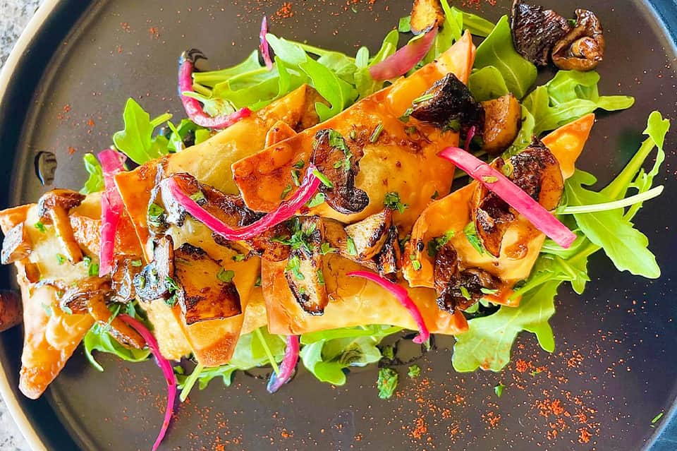 Grilled chicken and vegetable dish on dark plate with colorful garnish