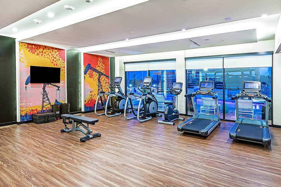 Modern fitness center with treadmills, exercise bikes, and city skyline views through windows