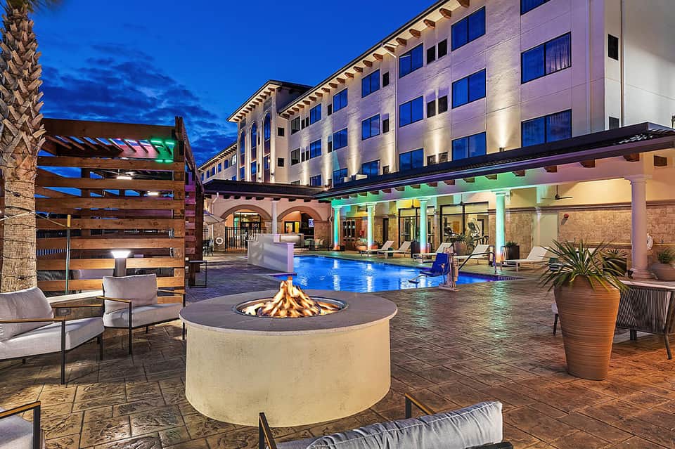 Resort courtyard at dusk with illuminated swimming pool, fire pit, and modern hotel building