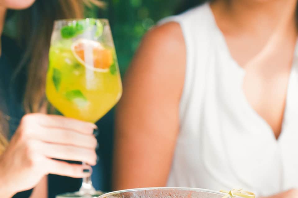 Person in white top holding yellow cocktail with fresh citrus and mint garnish outdoors