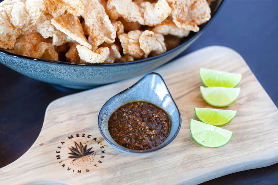Bowl of tortilla chips with salsa and lime wedges on wooden serving board