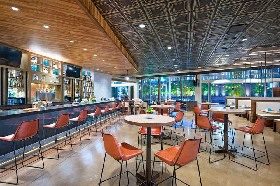 Contemporary bar and lounge with orange leather chairs, dark wood ceiling, and ambient lighting