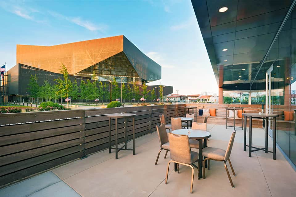 Modern waterfront terrace with round tables, chairs, and architectural building with orange copper facade