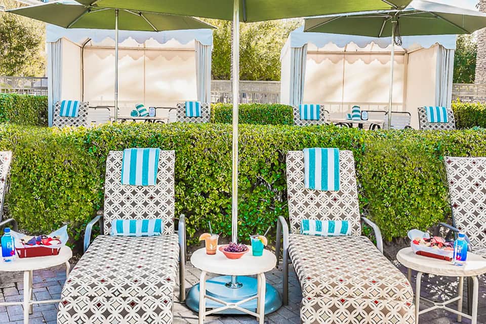 Luxury poolside cabanas with turquoise striped cushions under green umbrellas and cream privacy screens