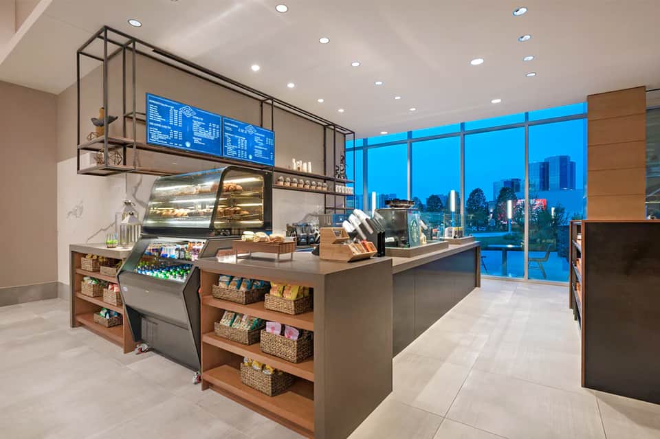 Modern hotel café with floor-to-ceiling windows, blue city skyline view, and espresso bar counter