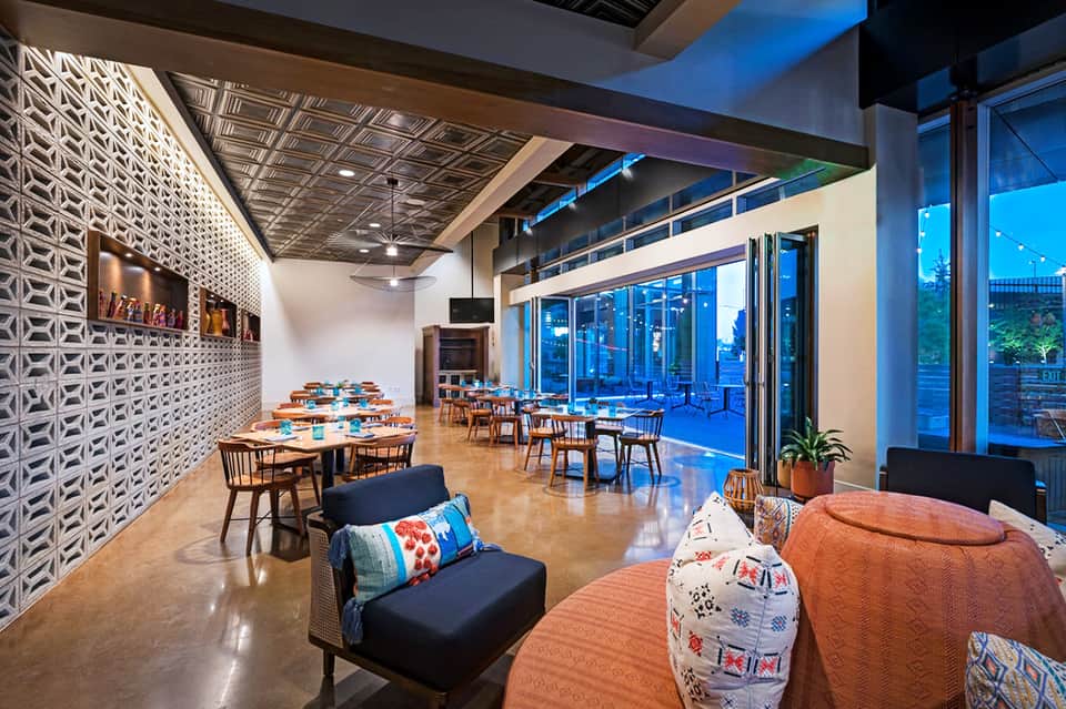 Modern restaurant and lounge with geometric wall panels, floor-to-ceiling windows, and city views