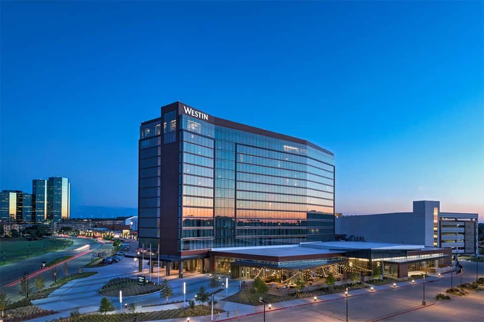 The Westin hotel exterior at dusk with glass facade reflecting sunset and illuminated courtyard