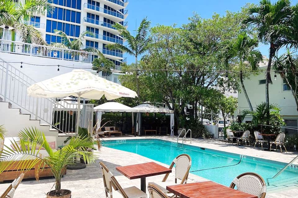 Resort pool deck with lounge chairs, white umbrellas, modern building, and tropical palm trees